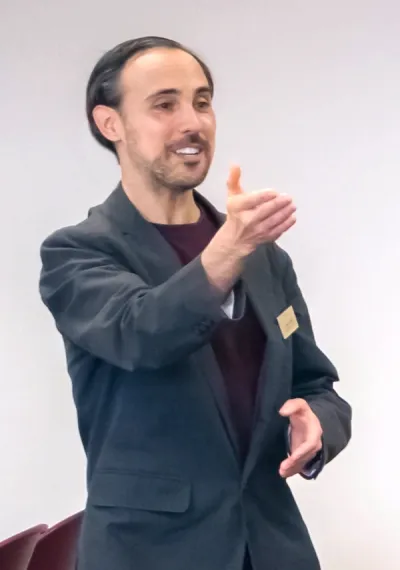 This is a tightly cropped photo of Professor Annelli interacting with students in a small classroom setting. He is smiling and gesticulating with his arms and hands as though he has just invited the students out of frame to respond to a question posed in the target language and subsequently shares in the mutual satisfaction of their response.